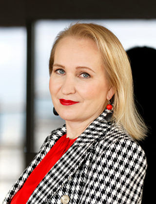 Teknologiateollisuuden varatoimitusjohtaja Minna Helle hymyilee punaisessa paidassa ja mustavalkoruudullisessa takissa.