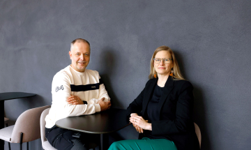 Capgeminin henkilöstöjohtaja Leena Kirjavainen ja luottamushenkilö Klaus West istuvat pienen mustan pöydän ääressä ja katsovat hymyillen kameraan.